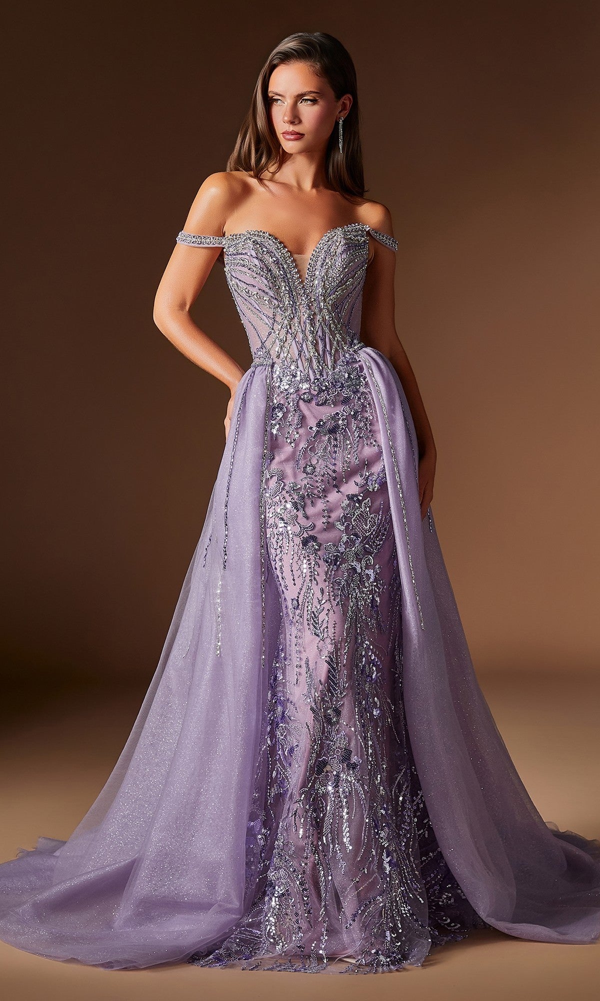 A woman models the Ladivine CDS570, a long off-the-shoulder lilac prom dress with silver embellishments, fitted bodice, and sheer flowing overskirt, standing against a plain brown background.